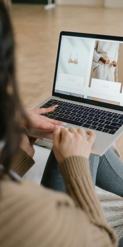Female browsing an online fashion store on a laptop indoors, focusing on clothing and accessories.